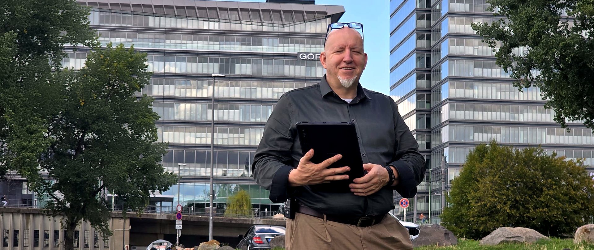Andreas Gerhardt vor einem Bürogebäude in Köln, mit Tablet